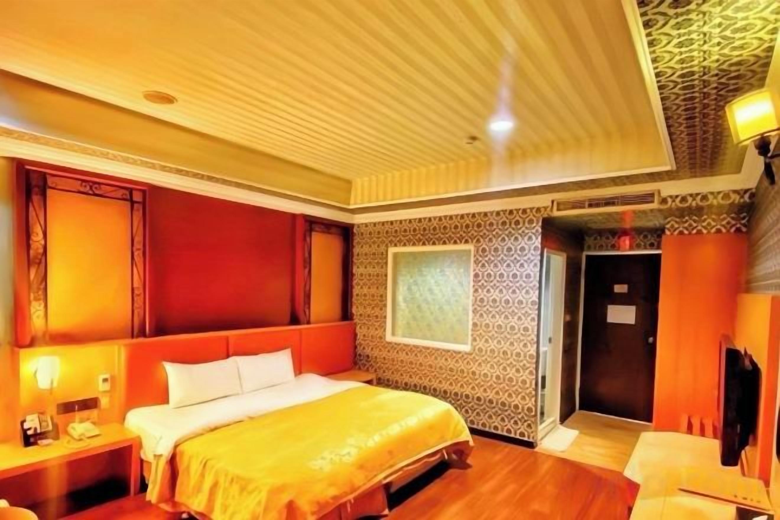 A hotel room with a large bed, a bedside table, a desk, and a patterned wall.