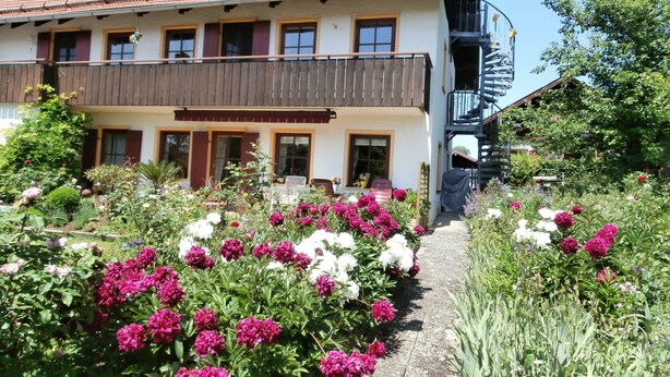 A two-story building with a balcony, a staircase, and a garden with various flowers. - Helles und gemütliches Dachstudio (Chieming)