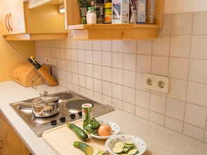 Een keuken met een fornuis, een snijplank, een messenblok en verschillende keukengerei.