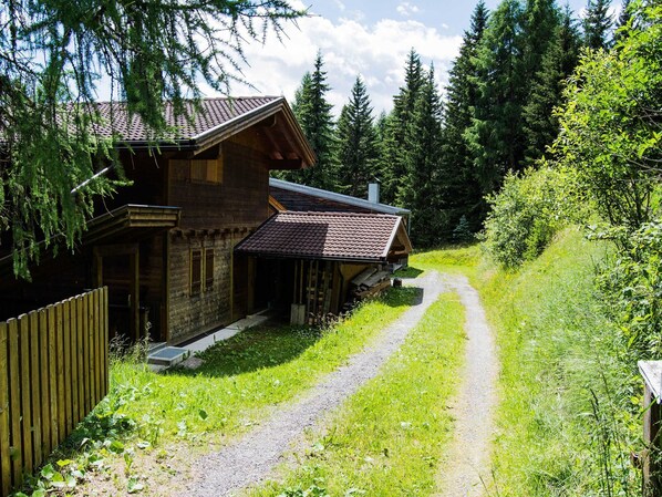 A wooden cabin with a sloped roof, a porch, and a gravel path leading to it.