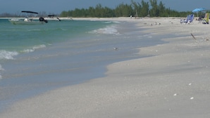 A beach with boats, a sandy shore, and a line of trees in the background. - A dream vacation at a low price: Get huge discounts on travel now! (Fort Myers)