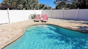 A swimming pool with clear blue water, surrounded by a white fence, and two red and white striped chairs. - A dream vacation at a low price: Get huge discounts on travel now! (Fort Myers)