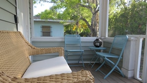 A wicker sofa and two blue chairs on a wooden deck with a view of a house and trees. - A dream vacation at a low price: Get huge discounts on travel now! (Fort Myers)