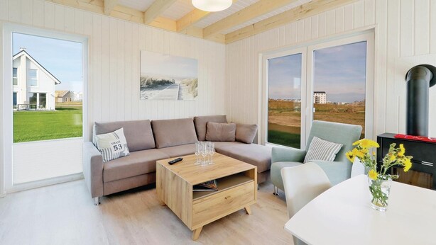 Ein modernes Wohnzimmer mit einem beigefarbenen Sofa, einem Holztisch und einem hellblauen Sessel. Ein großes Fenster bietet Blick auf ein Haus und eine grüne Wiese.