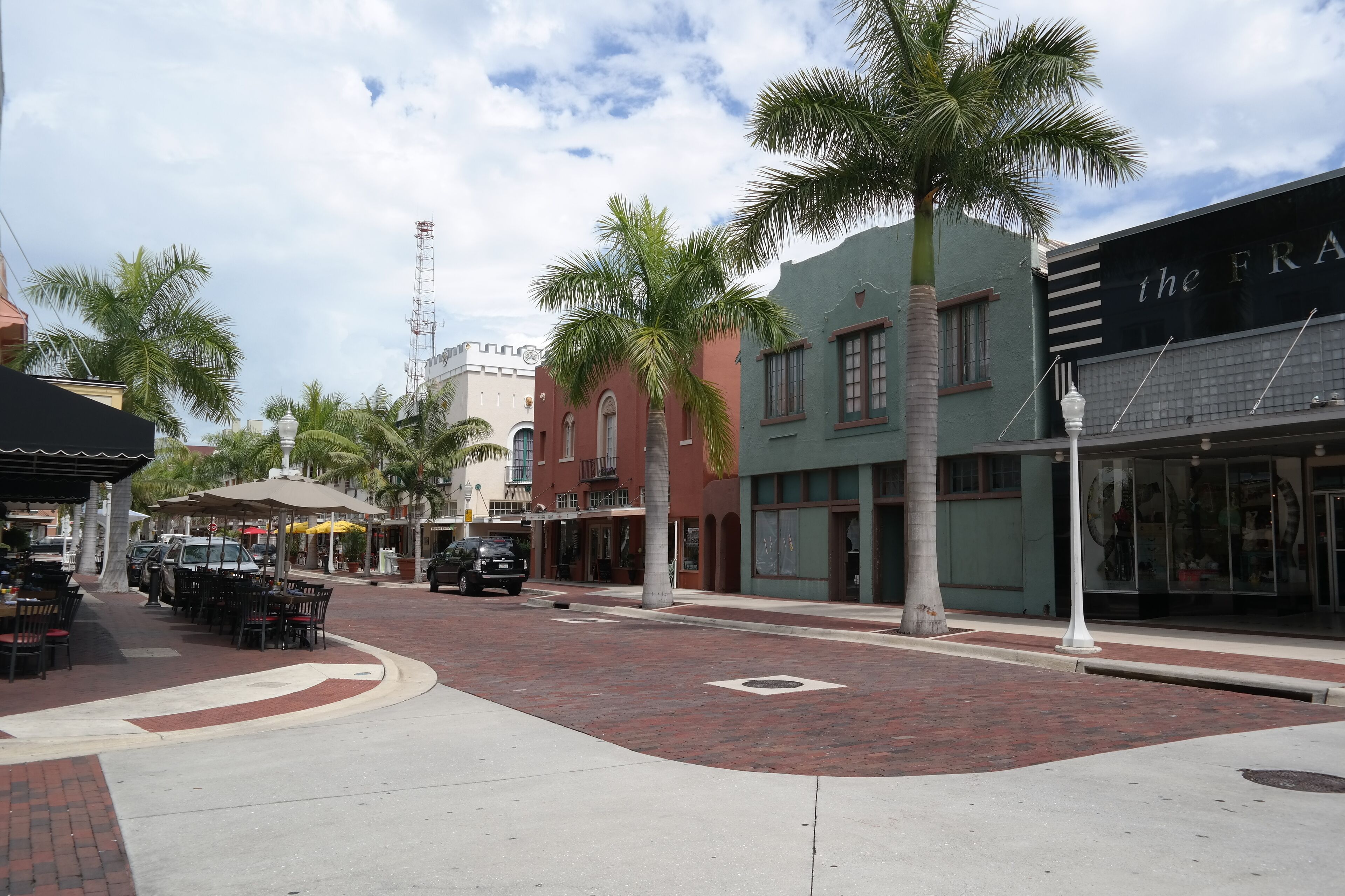 A street with palm trees, a restaurant with outdoor seating, and a building with a sign reading "the FRA".