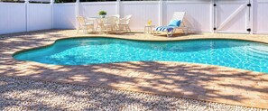 Une piscine avec une terrasse en briques, des meubles d’extérieur blancs et une clôture blanche.