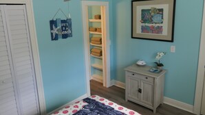 Ein Schlafzimmer mit einem Bett, einem Deckenventilator, einem Kleiderschrank, einem Regal mit Handtüchern und einem gerahmten Bild an der Wand.