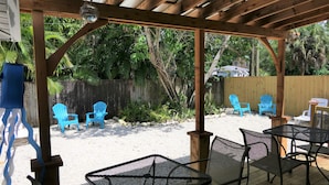 Ein überdachter Patio-Bereich mit einer Holz-Pergola, Metallstühlen und einem Tisch.