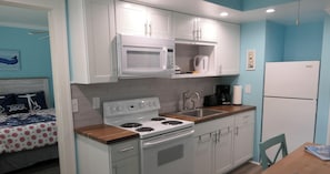 A compact kitchen with white cabinets, a microwave, a stove, and a refrigerator. - Travel Deals: Deeply discounted prices for your perfect vacation! (Fort Myers)