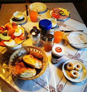 Une table de petit-déjeuner avec divers aliments, un verre de jus d’orange et un pot de Nutella.