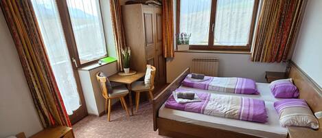 A room with two beds, a desk, a chair, and a radiator.