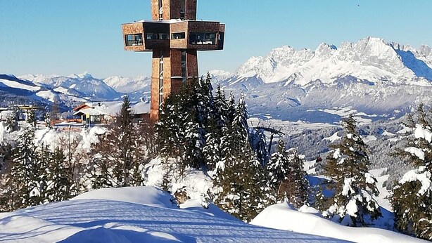 Paisatge nevat amb una estructura única en forma de creu al primer pla i muntanyes nevades al fons.