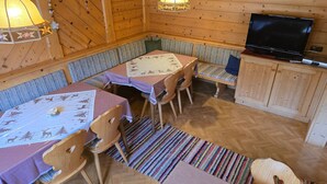 A cozy cabin interior with wooden walls, a dining table, benches, and a television.