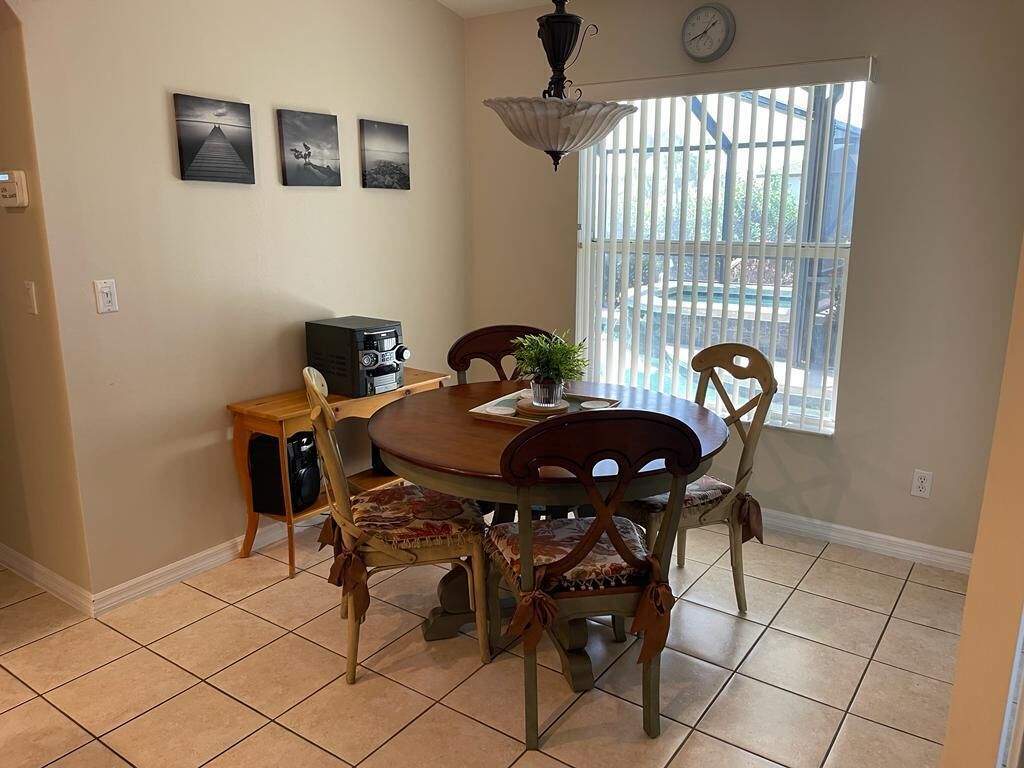 A dining area with a round table, four chairs, a small side table, a plant, and a clock on the wall.