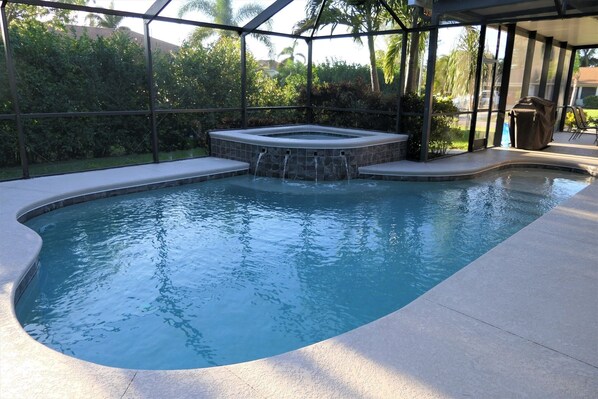 Una piscina con un jacuzzi, rodeada por un área de patio techada.