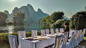 A dining table set up outdoors with chairs, overlooking a river and mountains. - Yangshuo Mountain Retreat (Guilin)