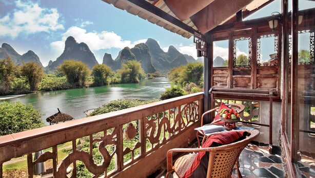 A balcony with a view of a river and mountains, wicker furniture, and a table with fruit. - Yangshuo Mountain Retreat (Guilin)