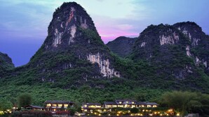 A hotel with traditional architecture, located near a body of water with reflections of the buildings. - Yangshuo Mountain Retreat (Guilin)