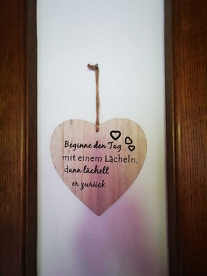 A wooden heart-shaped decoration with a message in German, hanging on a wall.