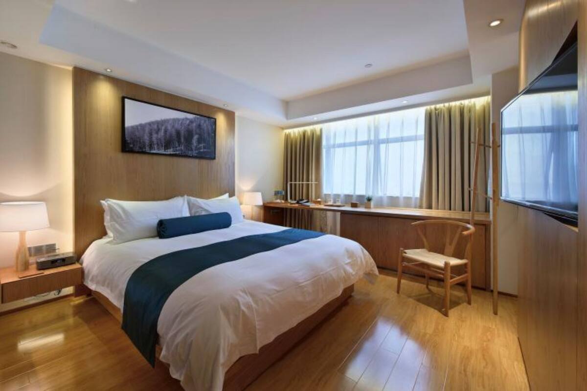 A modern hotel room with a large bed, a desk, a chair, and a TV.