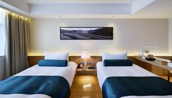 Habitación de hotel con dos camas, una mesita de noche, una lámpara, un escritorio con computadora y un cuadro en la pared.