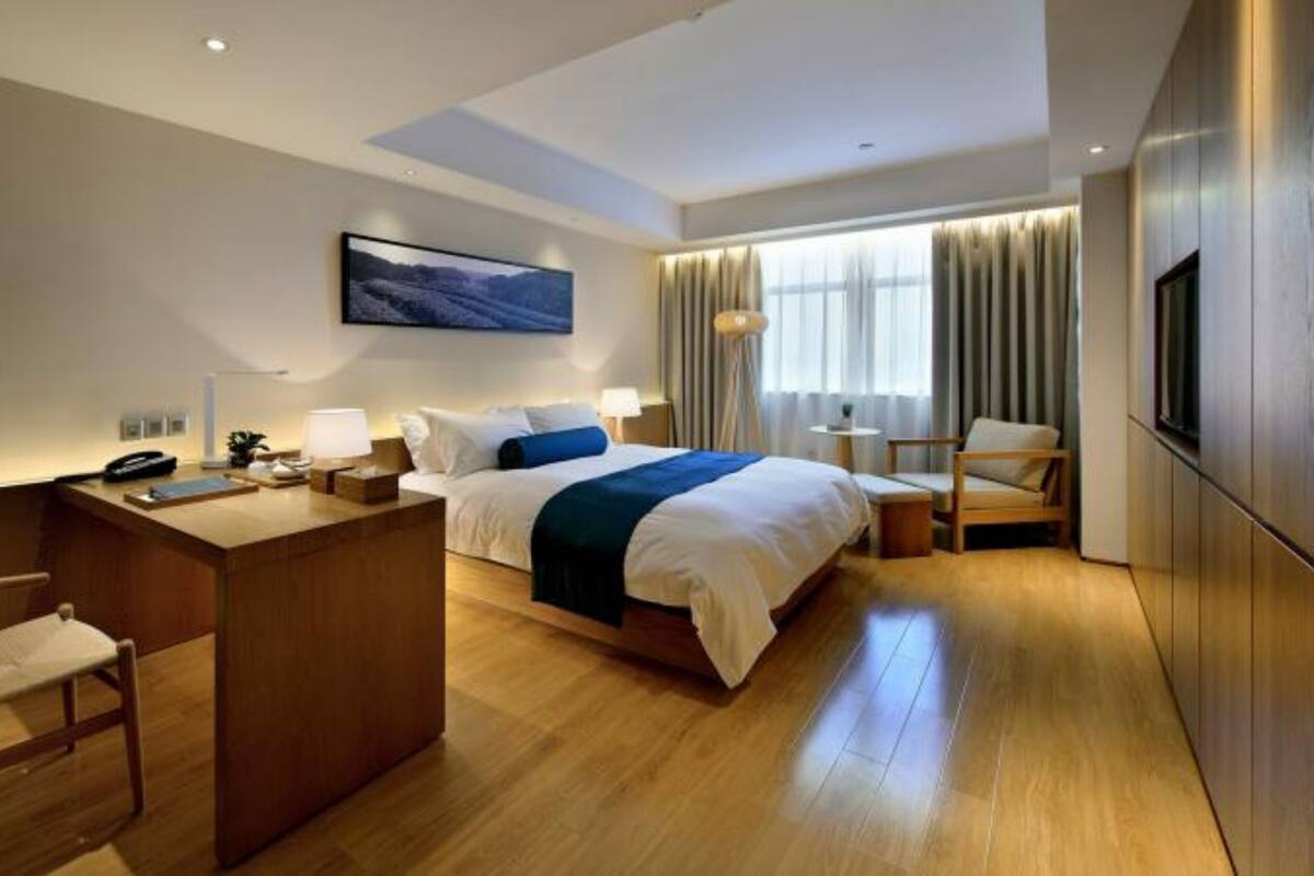 A modern hotel room with a large bed, a desk, a chair, and a TV.