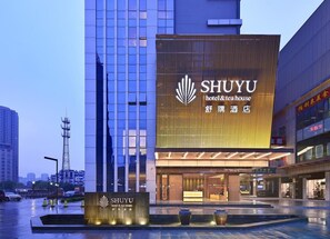 Un hotel con un gran letrero iluminado que dice "SHYU hotel & tea house" y una moderna fachada de vidrio.
