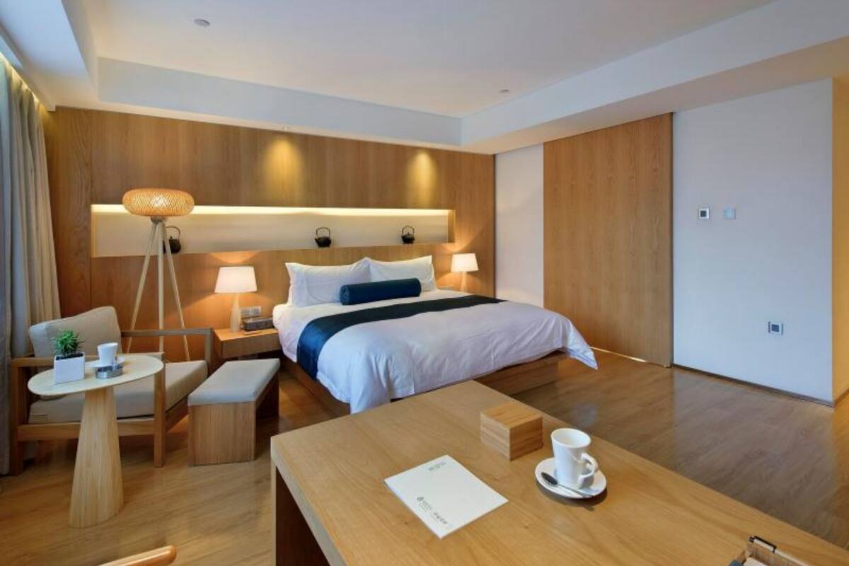 A modern hotel room with a large bed, bedside lamps, a small table with a cup, and a bedside plant.