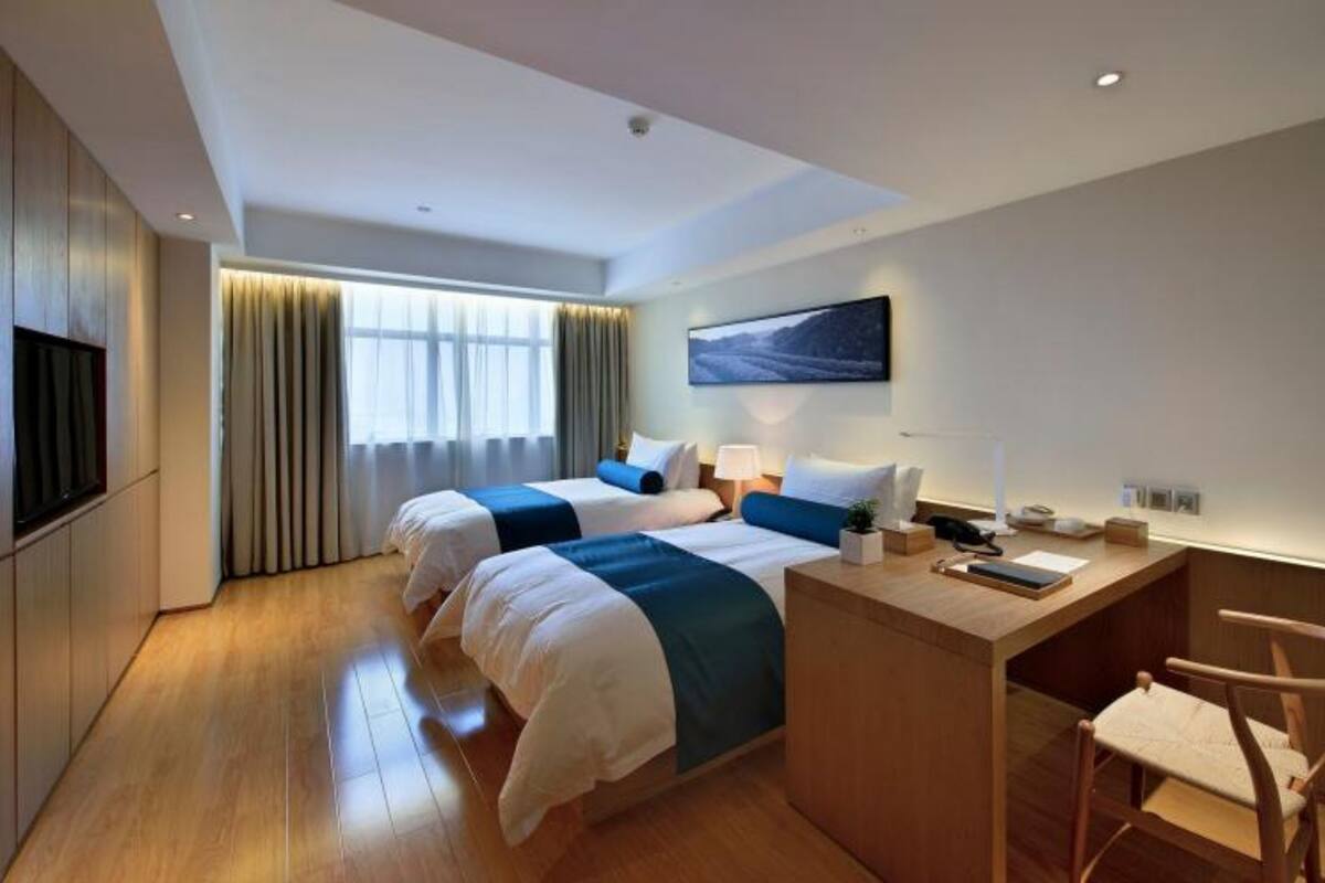 A hotel room with two beds, a desk, a chair, a TV, and a window with curtains.