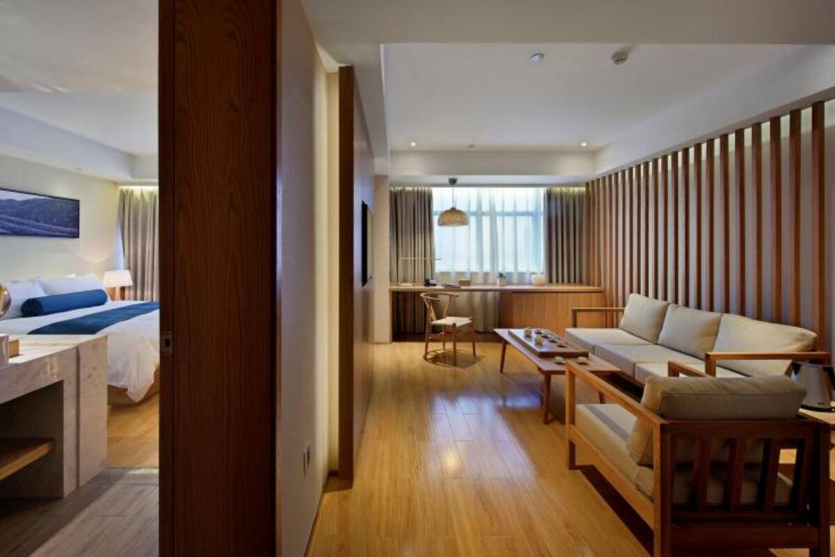 A modern hotel room with a bed, a desk, a sofa, and a dining area.