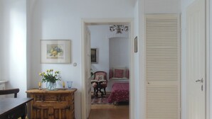 Un pasillo con suelo de madera, un candelabro, una puerta y una cama con colcha roja.