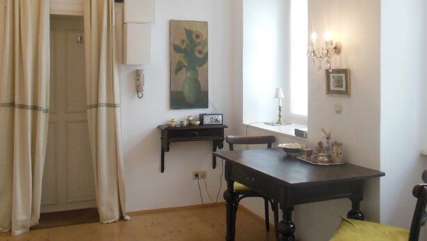 Un comedor con candelabro, una mesa, sillas, un cuadro y una ventana con cortinas.