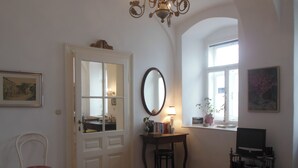 Una habitación con puerta, espejo, escritorio con lámpara, silla, estantería y televisor.