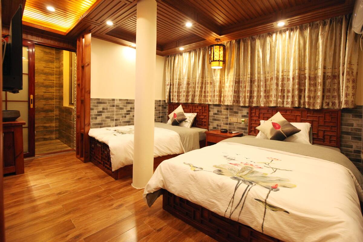A hotel room with two beds, wooden flooring, a brick accent wall, and a traditional Asian-style curtain.