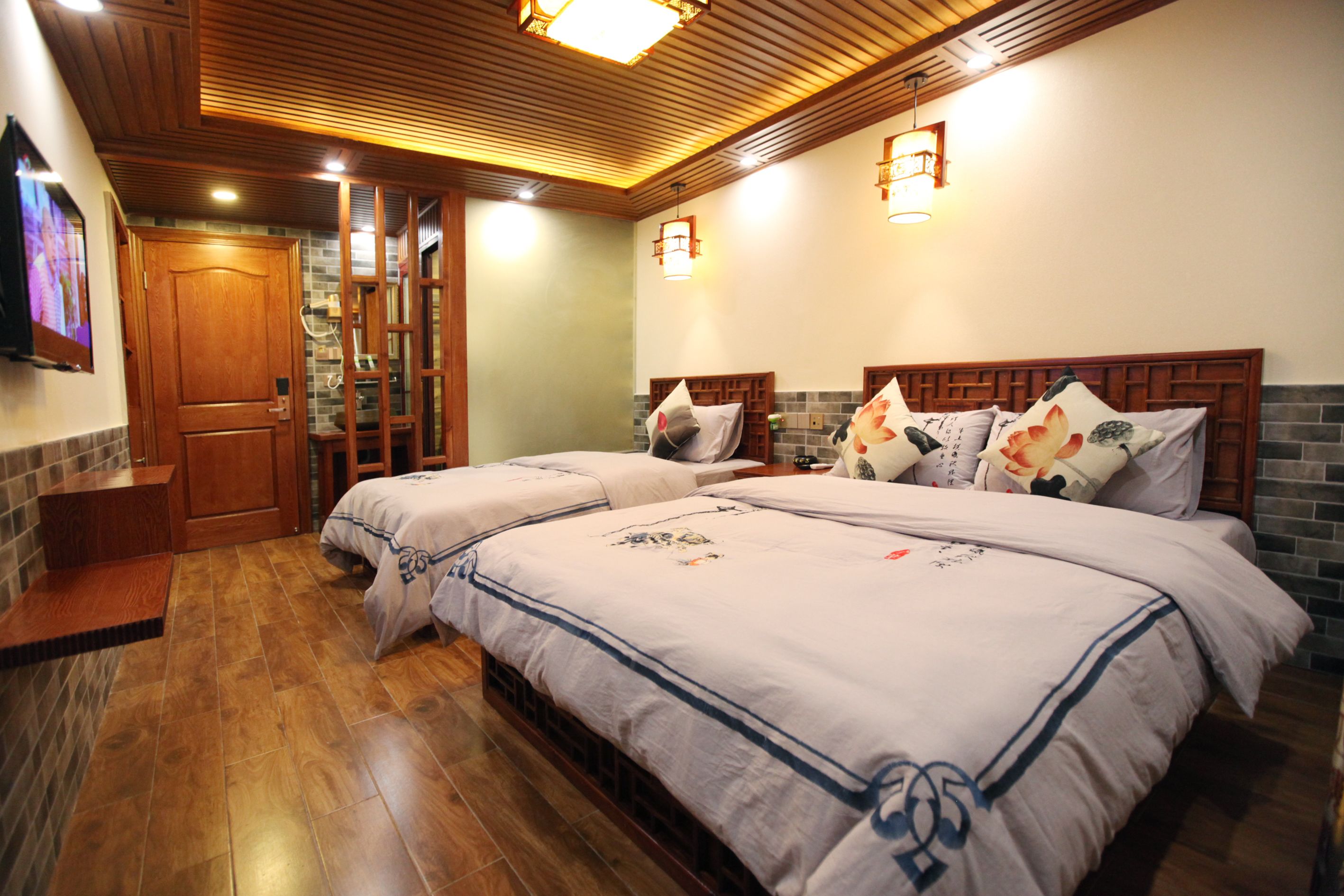 Quarto de hotel com duas camas, piso de madeira, porta de madeira e televisão na parede.