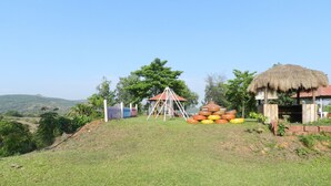A grassy area with a play structure, a thatched-roof shelter, and a pile of tires. - Hotel Sawai Mansing Hill Resort (Shahuwadi)
