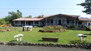 A stone building with a red roof, a covered porch, and a garden with flowers and rocks. - Hotel Sawai Mansing Hill Resort (Shahuwadi)