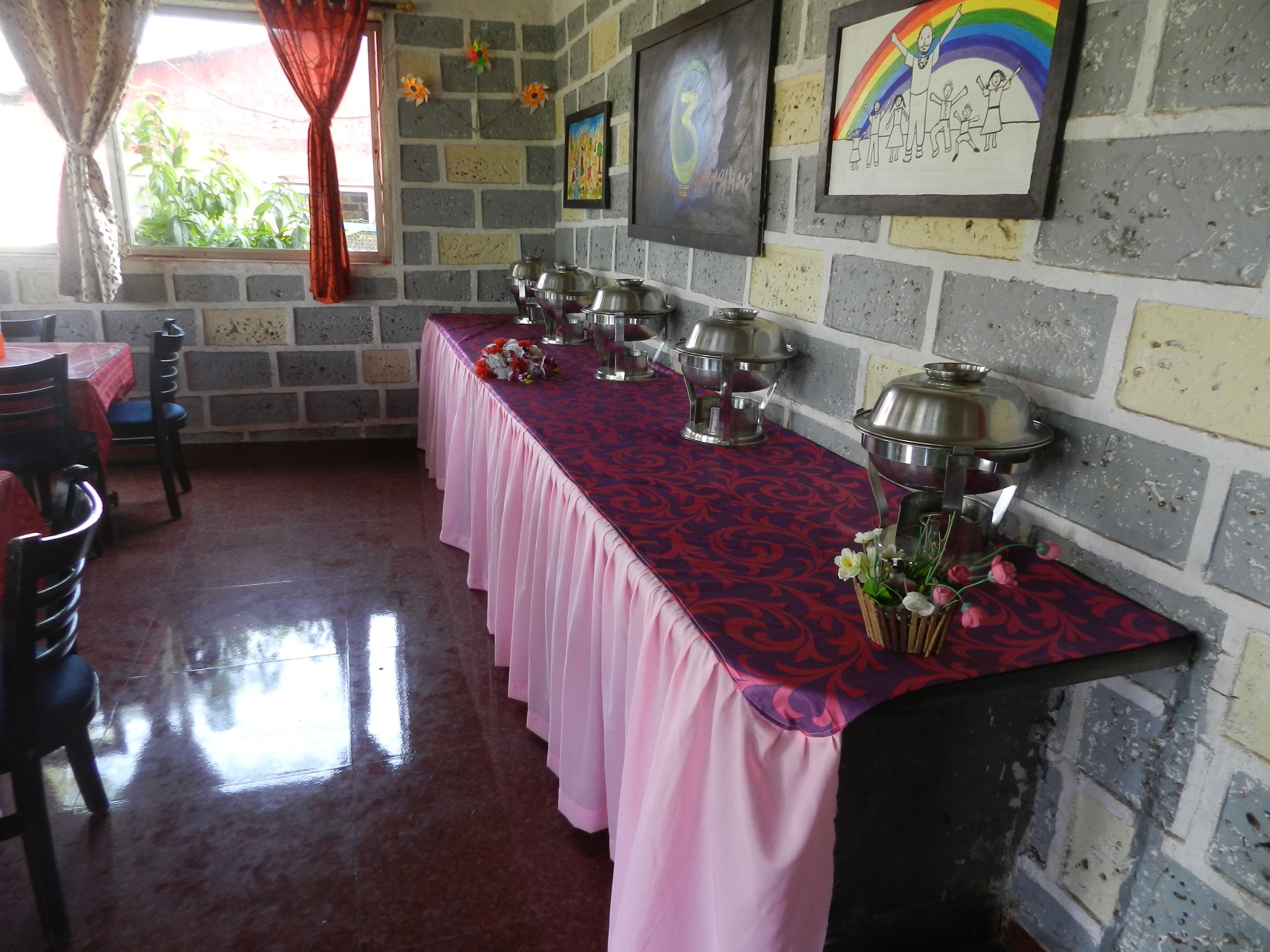 Un espace repas avec une longue table recouverte d’une nappe rose, entourée de chaises.
