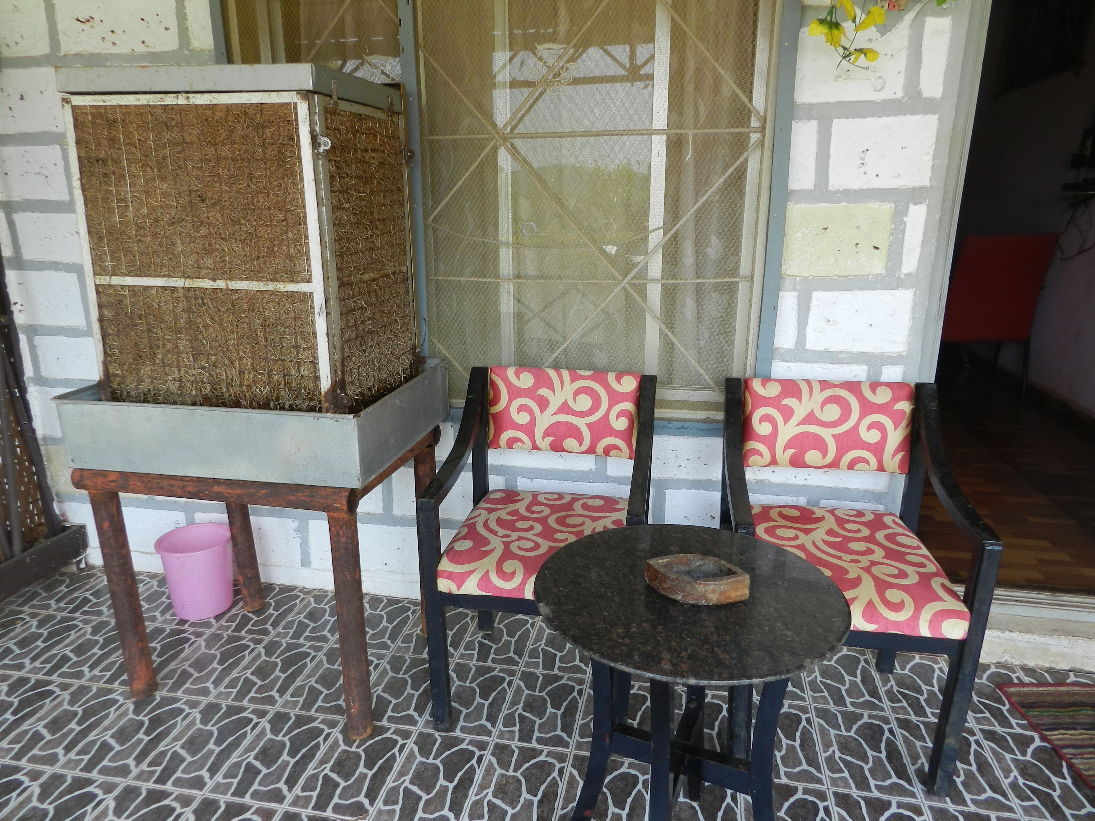 A room with a tiled floor, two patterned chairs, a small round table, and a large metal box on a stand.