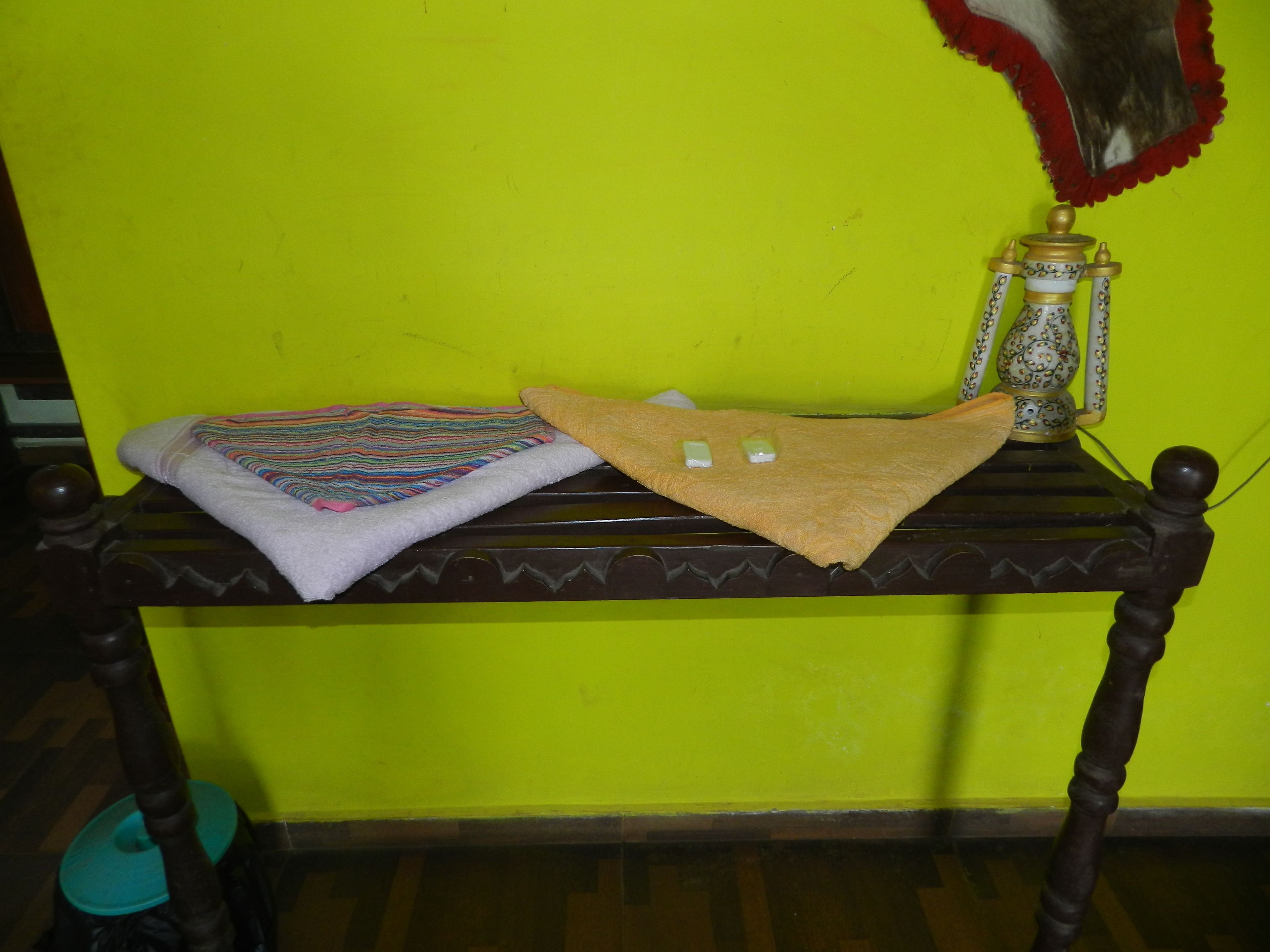 A wooden bench with a colorful blanket and a small decorative item against a bright green wall.