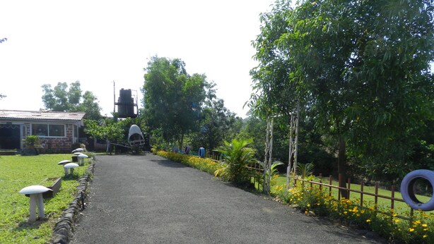 A pathway leading to a building with a brick facade, surrounded by greenery and decorative elements like white mushroom-shaped objects and a tire fence. - Hotel Sawai Mansing Hill Resort (Shahuwadi)