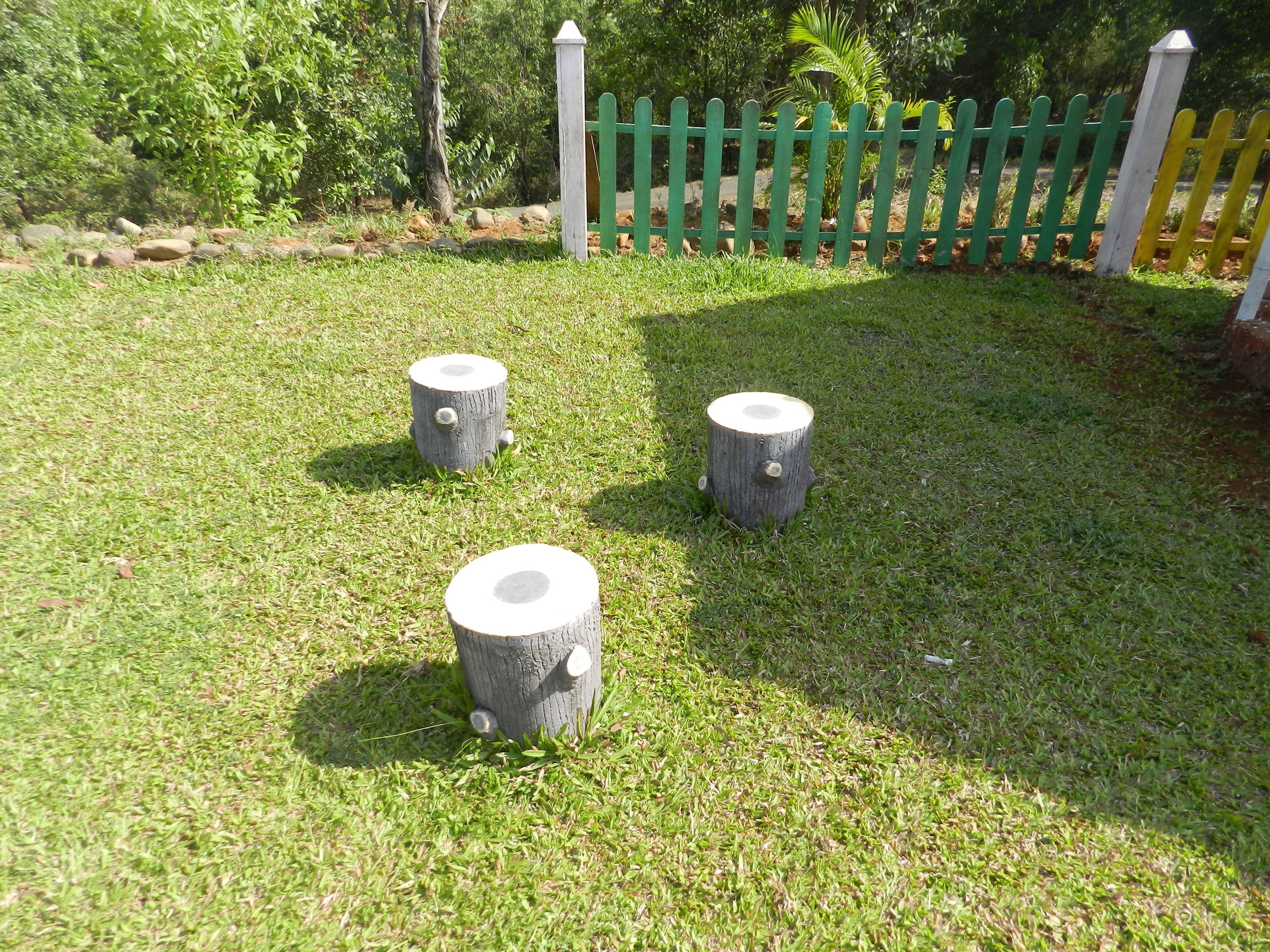 Three wooden posts on a grassy area with a green and white fence in the background.