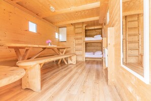 L’intérieur d’un chalet en bois, avec une table de pique-nique, des bancs, une petite fenêtre et un lit avec des oreillers.