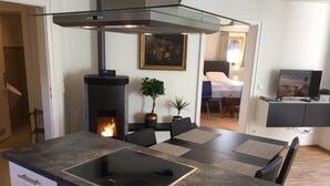 A modern kitchen with a built-in stove, a dining area with a table and chairs, a fireplace, and a television in the background.
