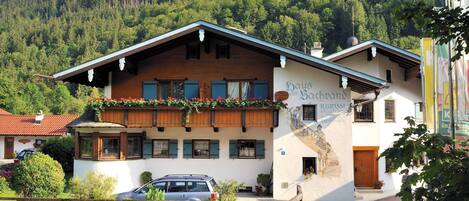 A traditional Alpine-style building with a wooden facade, a balcony with flowers, and a sign indicating it is a guesthouse.