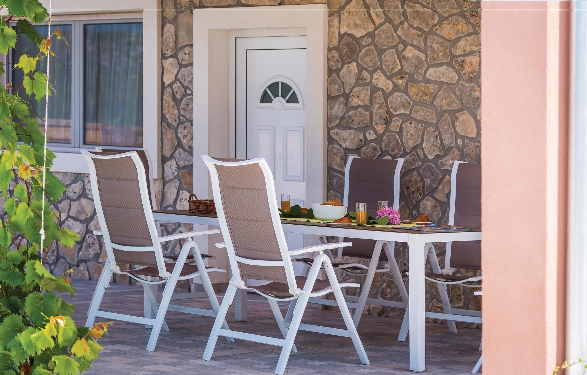 An outdoor dining area with white metal chairs and a table set for two.