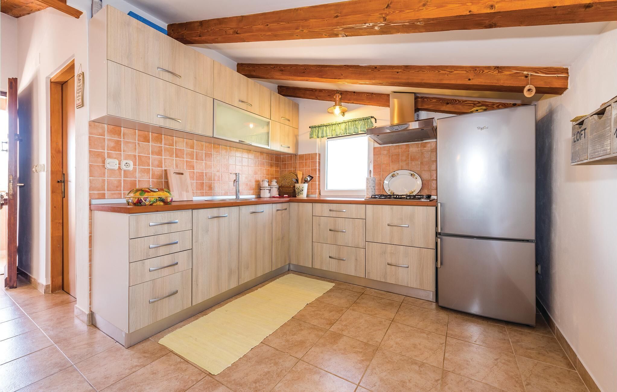 Eine Küche mit Holzausstattung, einem Edelstahlkühlschrank und einem Fenster mit kariertem Vorhang.