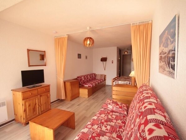A living room with a sofa, a TV, wooden furniture, and a painting on the wall.