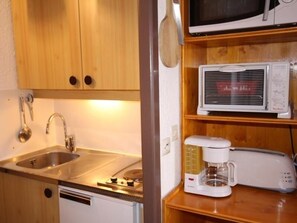 Uma cozinha compacta com armários de madeira, uma pia de aço inoxidável, micro-ondas e cafeteira.