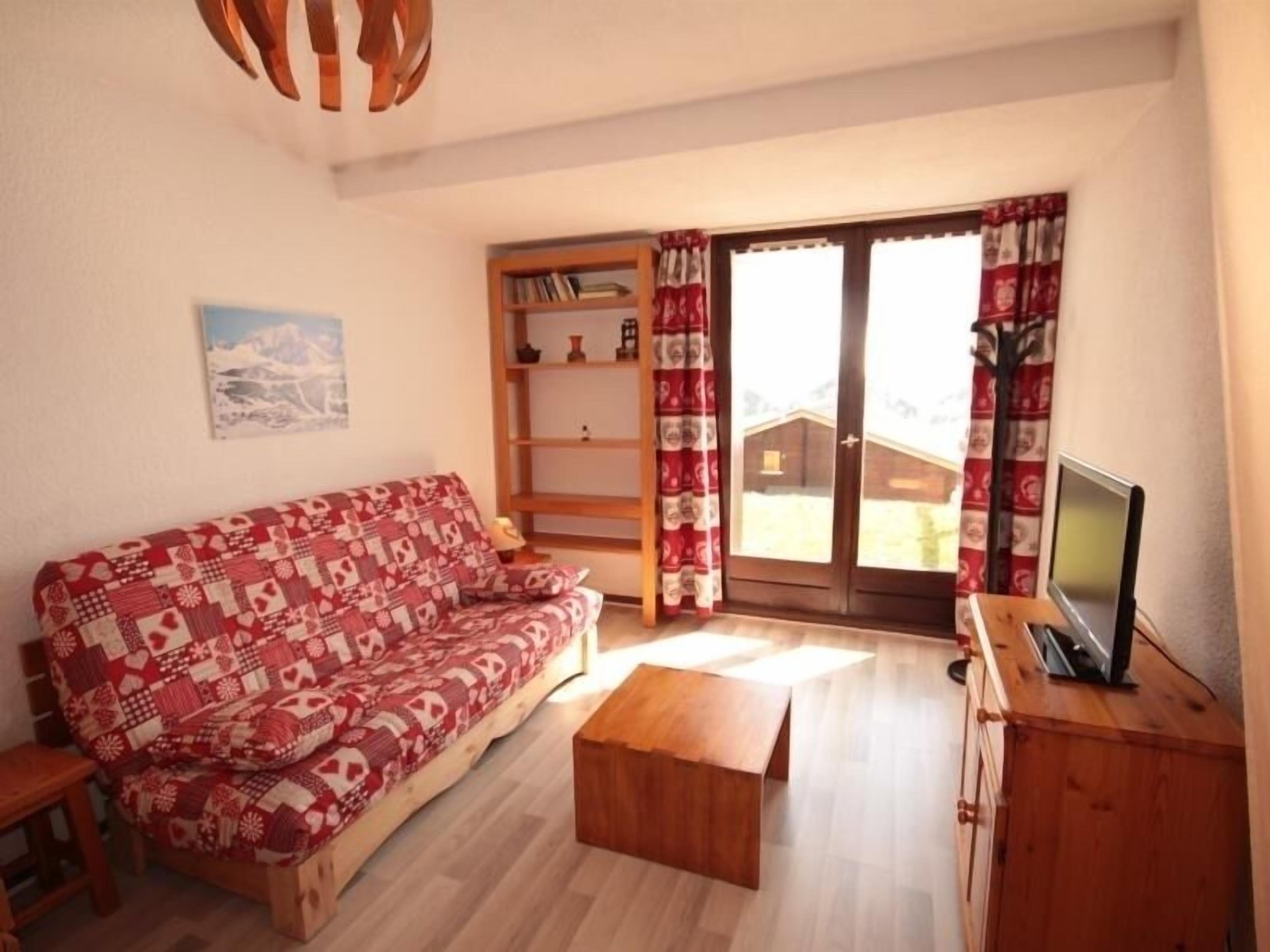 A cozy living room with a patterned sofa, a wooden coffee table, and a TV on a wooden cabinet.